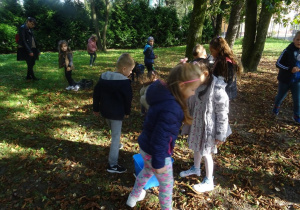 Dzieci spacerują z pochyloną głową po parku w poszukiwaniu kasztanów.